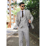 Man in a gray suit walking outdoors with buildings and greenery in the background