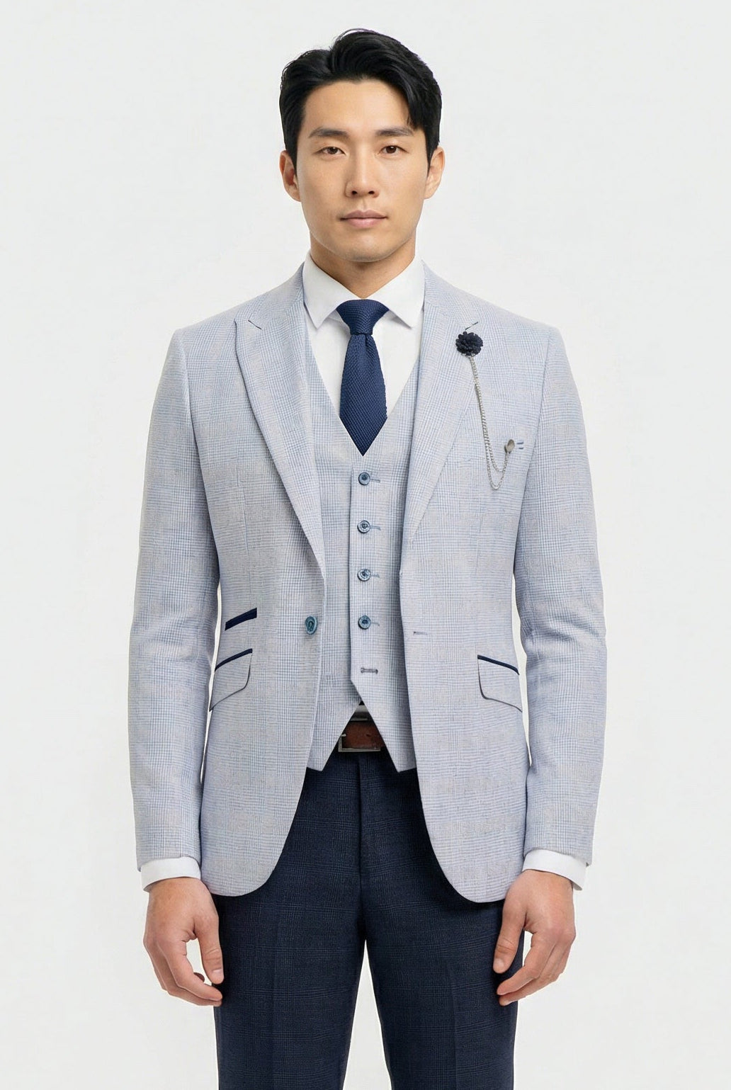 Man wearing a light gray blazer, navy vest, and dark blue tie on a white background