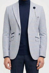 Man wearing a light gray blazer, navy turtleneck, and dark pants on a white background